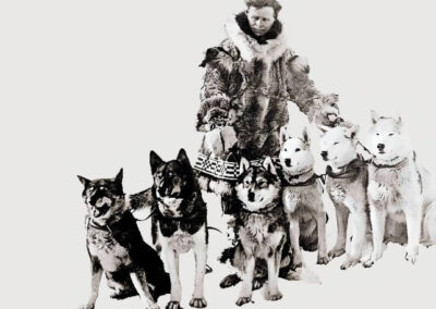 Black-and-white photograph of Leonhard Seppala, dressed in fur-lined arctic gear, standing with his team of Siberian huskies, including the famous sled dog Togo.